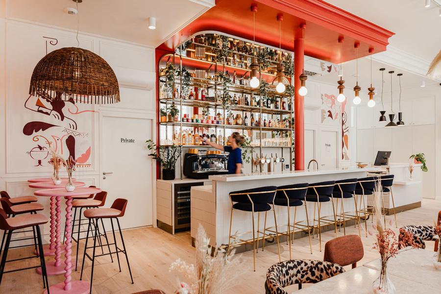 L'espace bar, avec un mur de bouteille et de décoration à l'arrière, des chaises hautes devant le bar, et sur le côté des tables et chaises hautes.