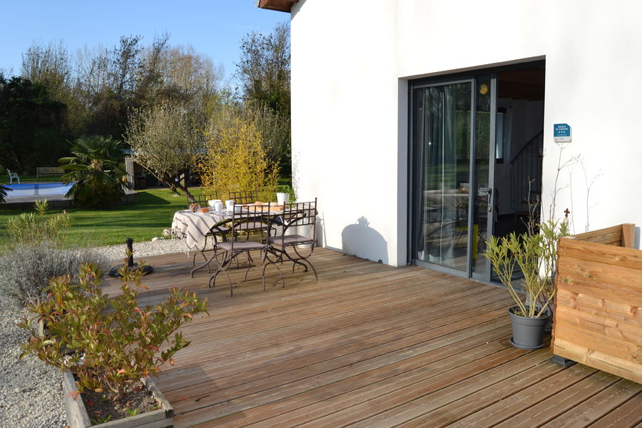 Terrasse avec table dt chaises, jardin arboré et piscine au fond