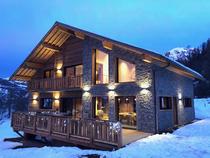 Grand chalet en bois et pierre sur deux étages, nombreuses fenêtres et large terrasse, balcon au 1er étage