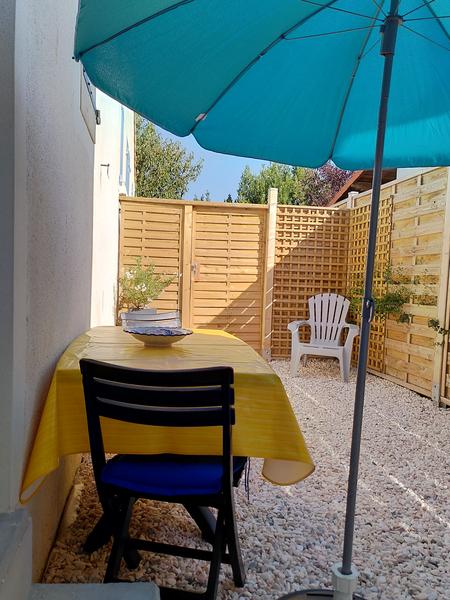 petite terrasse avec palissade en bois, une table deux deux chaises, un parasol.