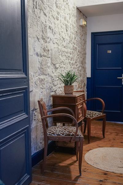Deux sièges imitation giraffe avec petite table, dans un couloir aux murs en pierres, deux portes bleues.
