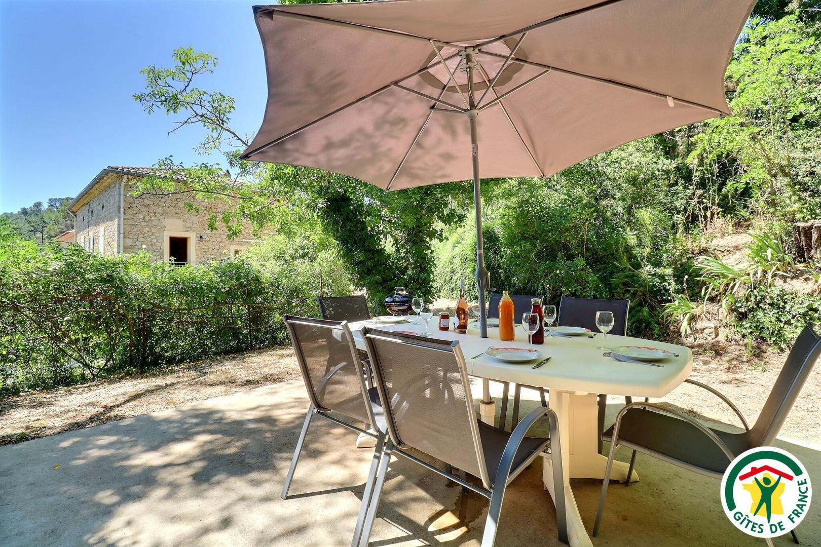 Terrasse privative avec salon de jardin et barbecue, à quelques mètres du gîte (on voit le gîte en arrière plan)