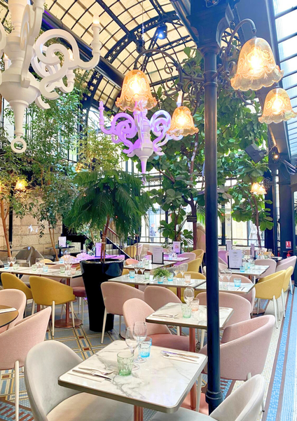 La salle avec des tables dressées, sous la verrière sous laquelle sont suspendus de grandes plantes.