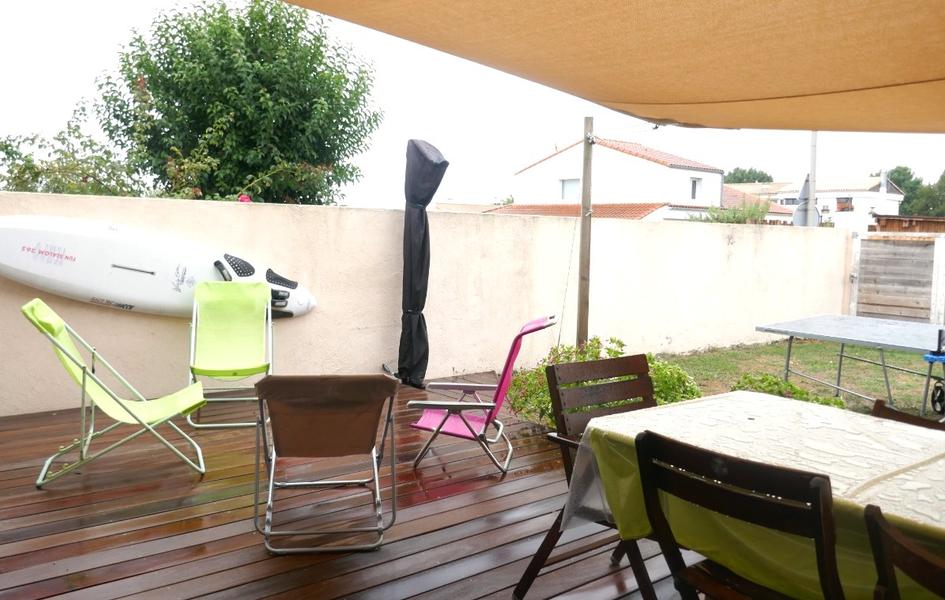 Une terrasse avec une table, 4 chiliennes, une planche de surf accrochée au mur, une table de ping pong.