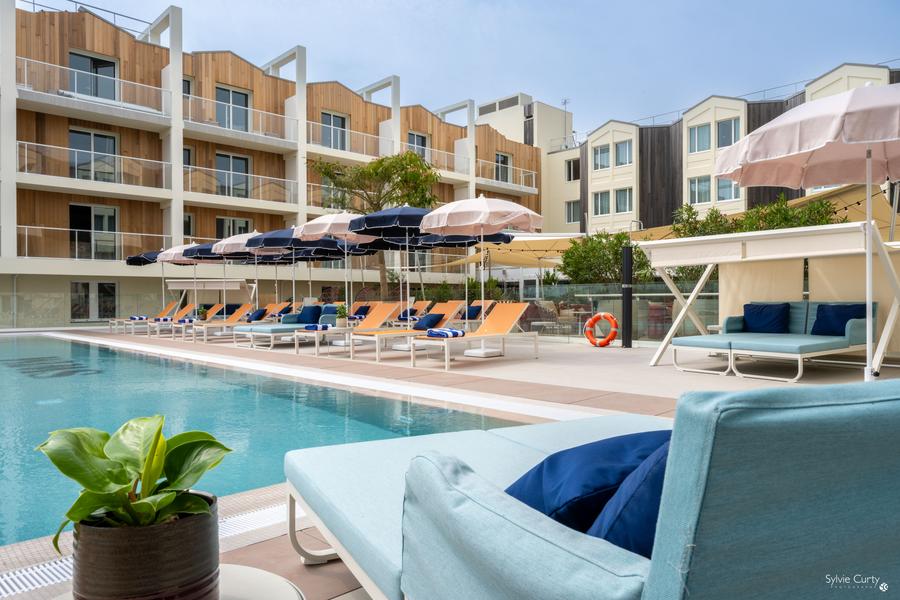 La piscine découverte entourée par les murs de l'hôtel, avec transats et parasols.