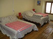 Chambre à coucher lumineuse avec deux lits doubles, ameublement bois, parquet au sol, fenêtre