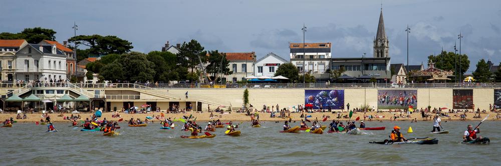 Vue sur une plage depuis l'océan, avec une cinquantaine de kayakistes.
