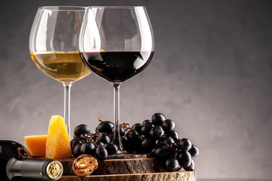 Image front-view-wine-glasses-fresh-grapes-walnuts-yellow-cheese-wood-board-overturned-bottle-dark-background