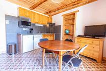 Séjour lumineux avec coin cuisine, plaques électriques, table à manger, TV, ameublement bois, sol carrelé