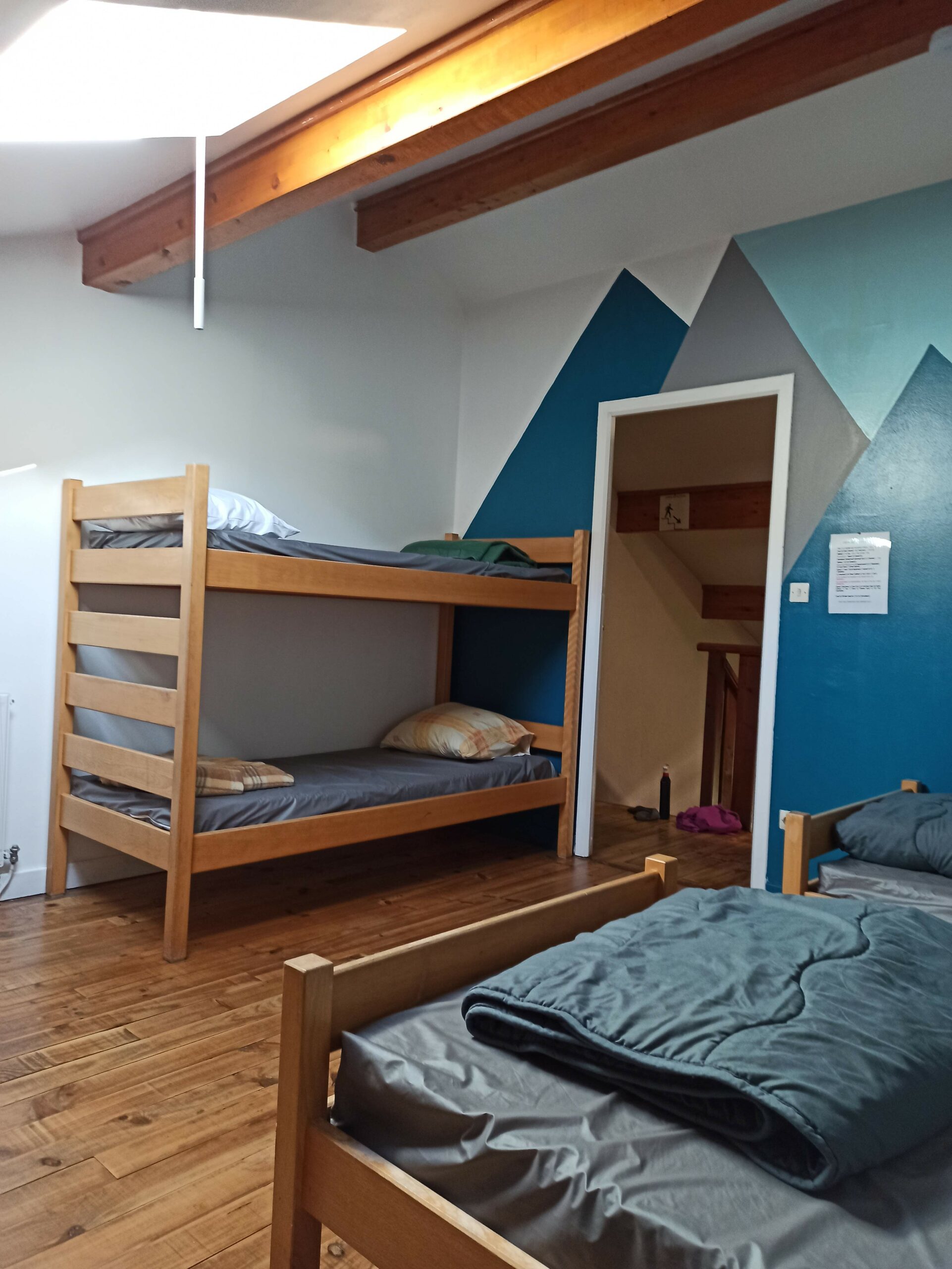 La chambre Vertaco du Gîte et auberge de Carri à La Chapelle en Vercors. Une chambre mansardée chaleureuse, avec lits superposés, murs bleus, mobilier en bois et lumière naturelle créant une ambiance conviviale.