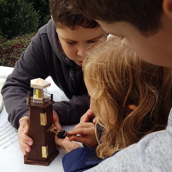 Deux enfants cherchant à ouvrir une boite en forme de phare fermée à clef.