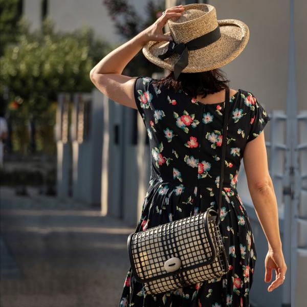 Une dame avec un chapeau de dos portant un sac en bandoulière.