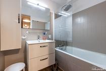 Salle de bains moderne et carrelée avec baignoire, évier et miroir, placard