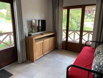 Séjour lumineux de l'appartement avec canapé, TV, ameublement bois, fenêtre et porte-fenêtre donnant sur une terrasse en bois