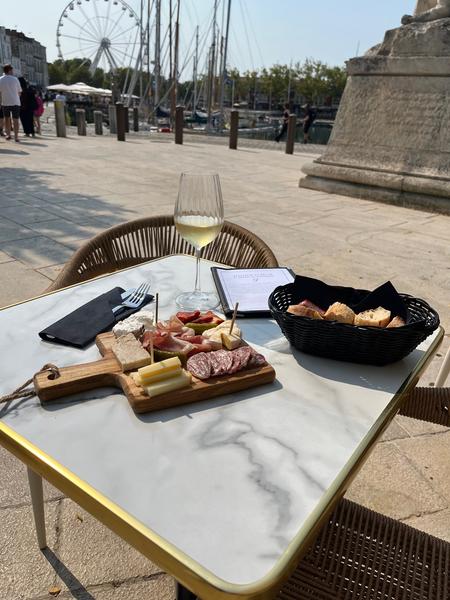 Une table en terrasse avec une planche de charcuterie et fromages, et un verre de vin.