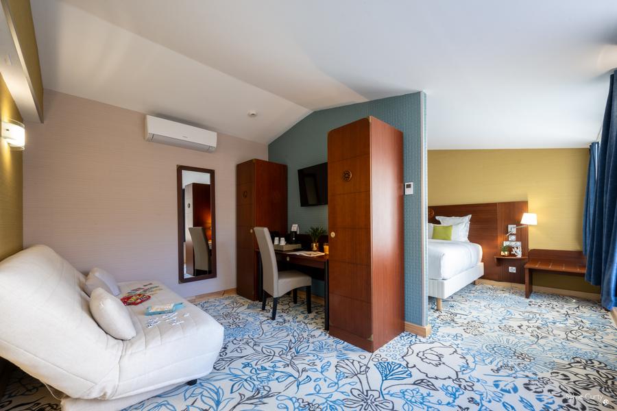 Une chambre séparée par un demi-mur, avec un lit double, un canapé avec des jeux de cartes, une télévision, un bureau et une chaise, deux armoires.