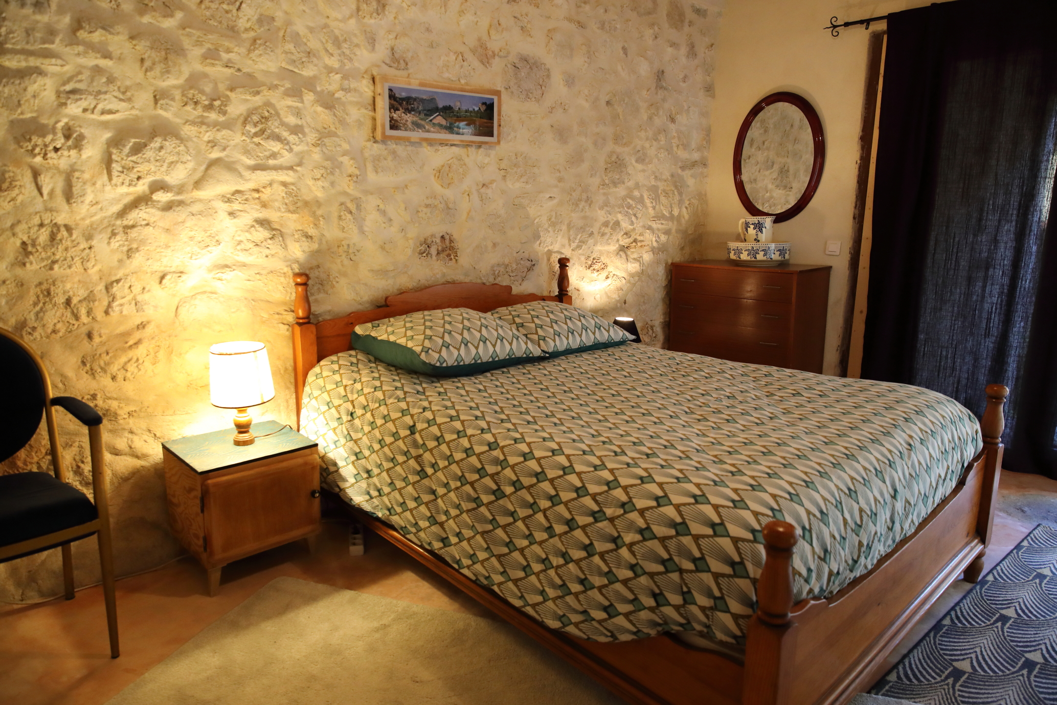 hambre rustique et chaleureuse avec lit double, murs en pierre, poutres apparentes, éclairage tamisé, mobilier ancien et décoration sobre.