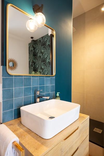Un évier, un miroir, et un carrelage au mur bleu.
