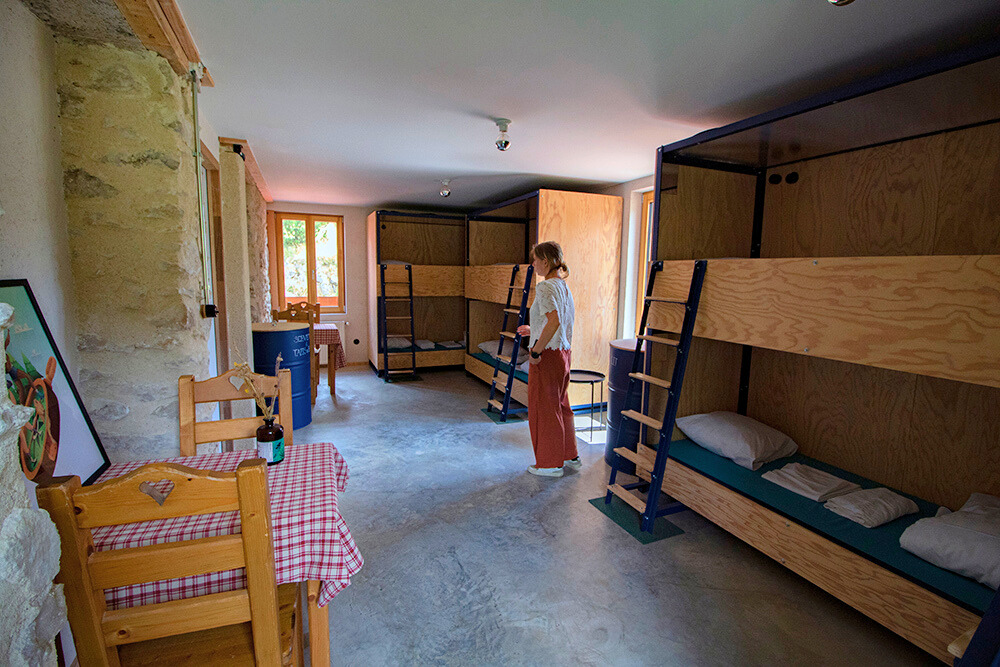 Sur la droite, 3 des 4 lits à étages qui composent le dortoir de 8 places. A gauche 2 tables en bois avec des chaises.