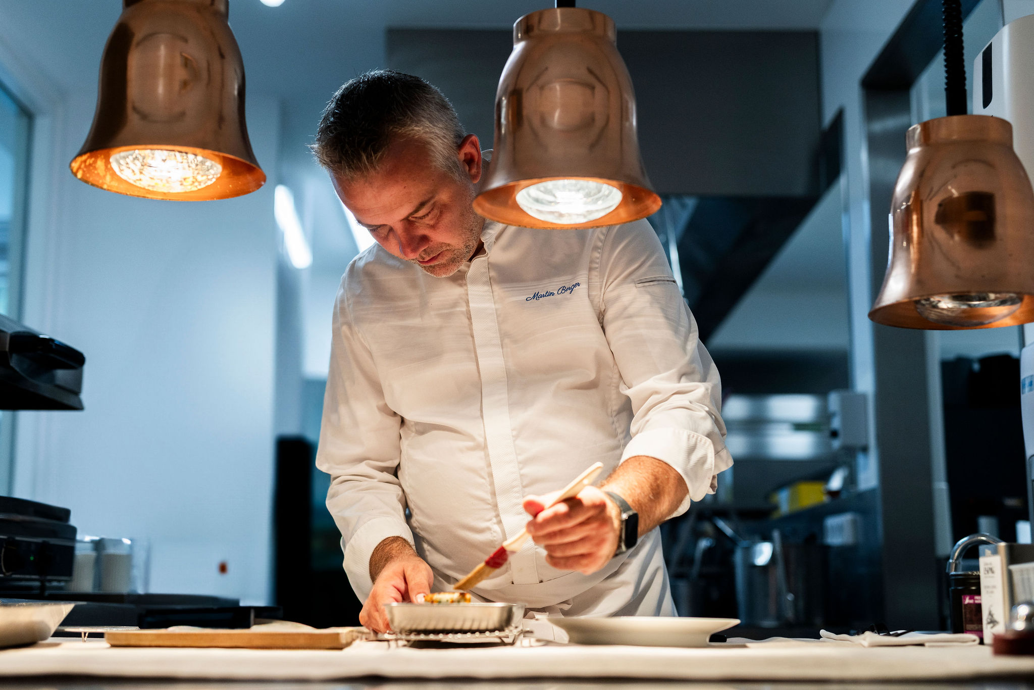 Portrait de Martin Berger, chef de la Table d'Uriage, dressant un plat dans sa cuisine.
