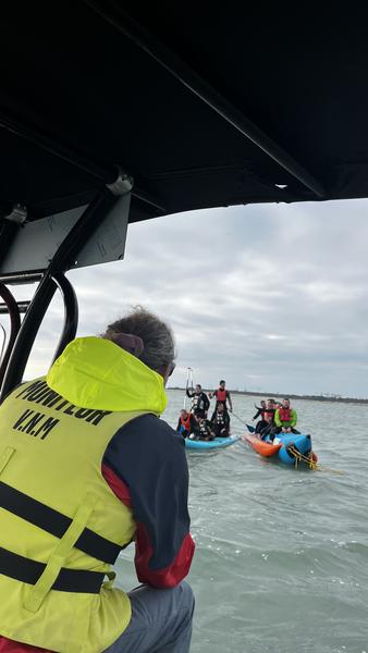 Le moniteur de dos sur un bateau, en fond un groupe sur une bouée tractée banane et un paddle géant.