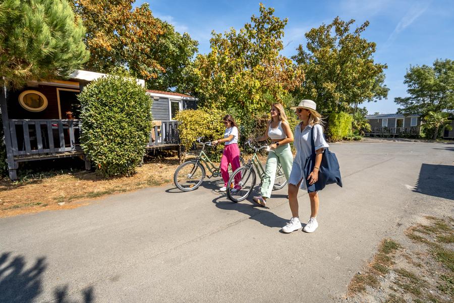 trois dames dont deux faisant rouler un vélo, marchant dans les allées du camping.