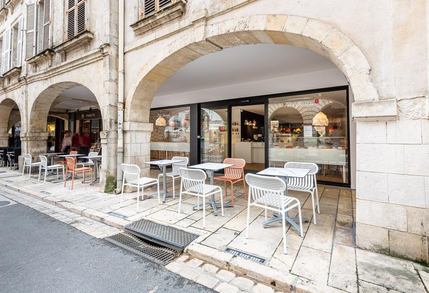 Vue extérieure de la pâtisserie, sous les arcades, avec des tables et des chaises installées dehors