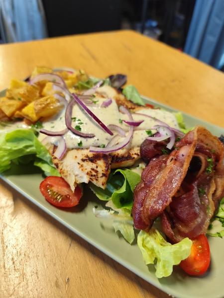 une salade avec salade, bacon, tomates, sauces, oignons, etc.