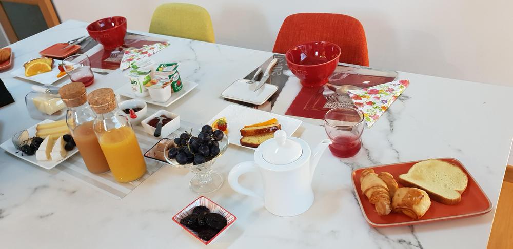 Un petit-déjeuner avec du jus de fruits, de fromages, des yaourts, des viennoiseries, des fruits, des bols et des verres.
