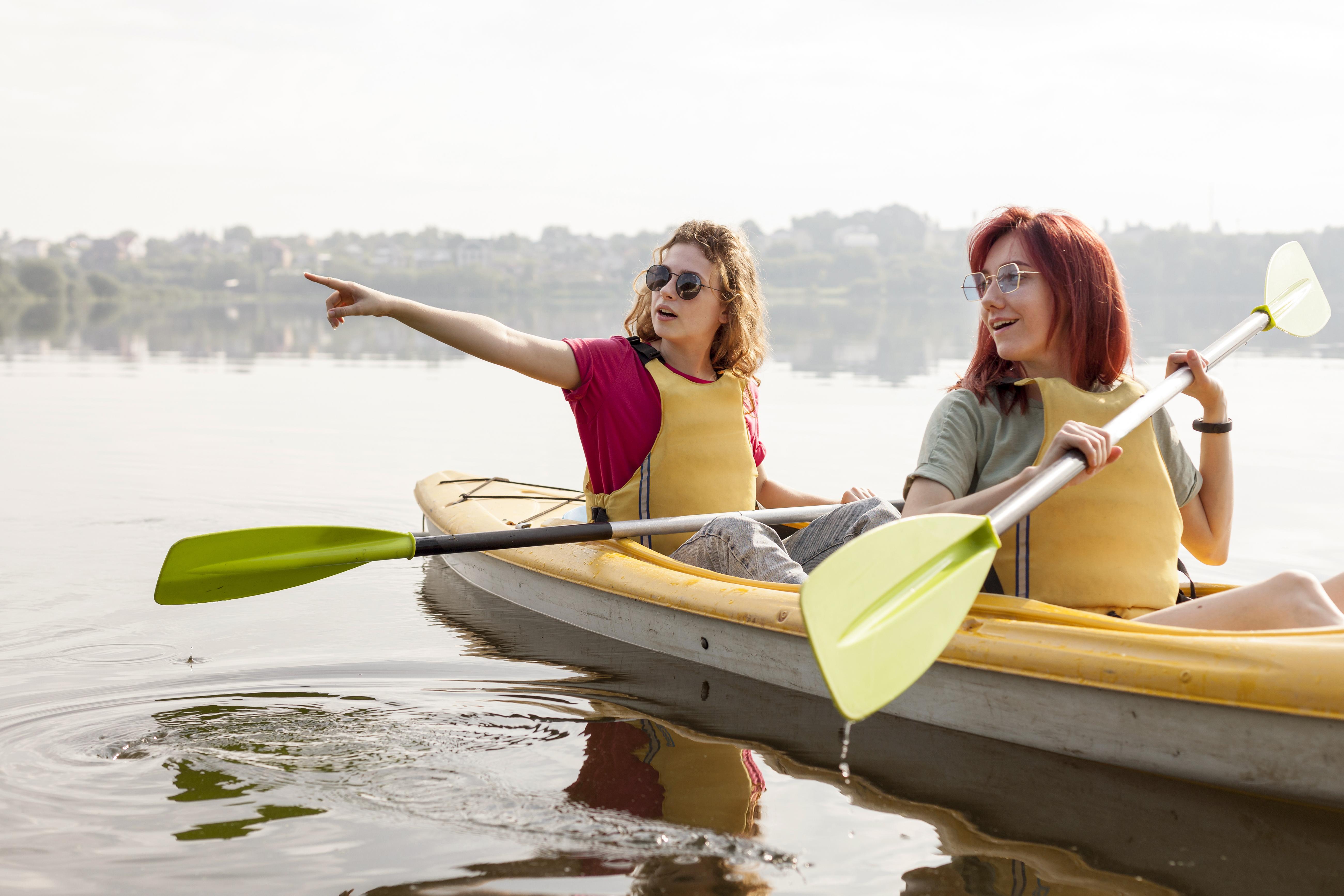 Amies souriantes en train de faire du Canoë sur le lac qui montrent quelque chose du doigt