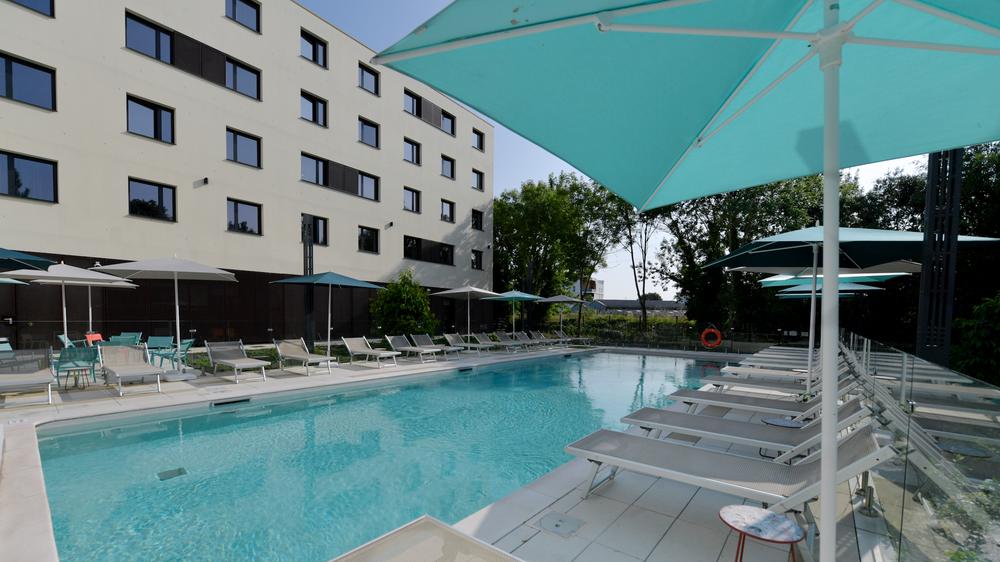 La piscine extérieure découverte de l'hôtel, l'hôtel en fond, des parasols et transats.