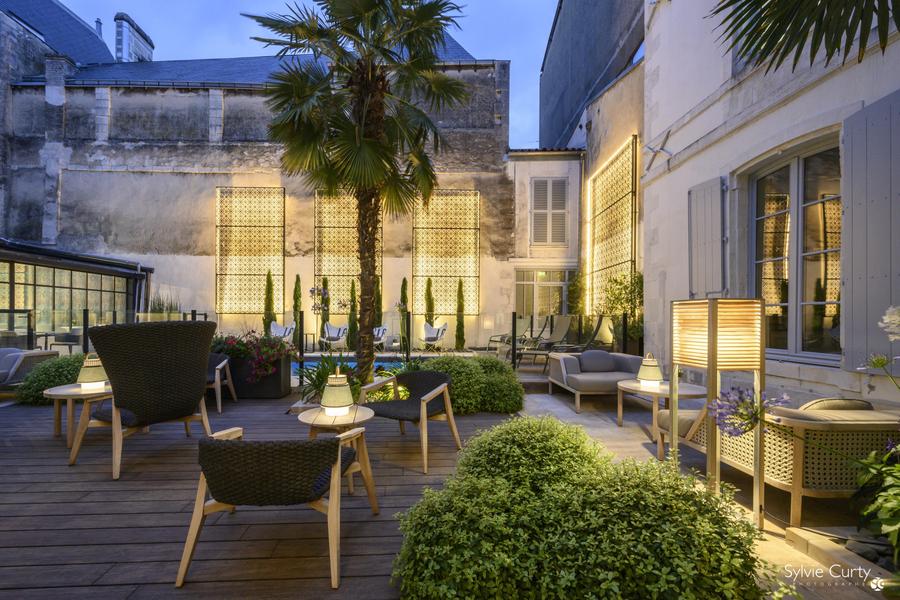 Cour intérieure avec tables et chaises, végétation et lumière tamisée