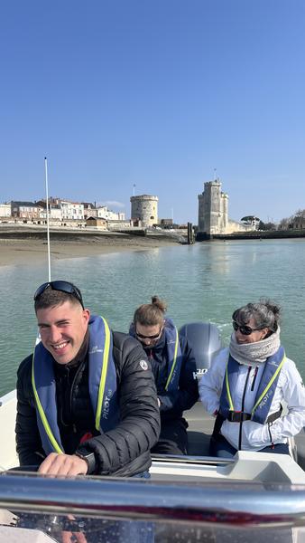 Trois personnes sur un bateau à moteur quittant le port, en fond les Tours de la Rochelle.