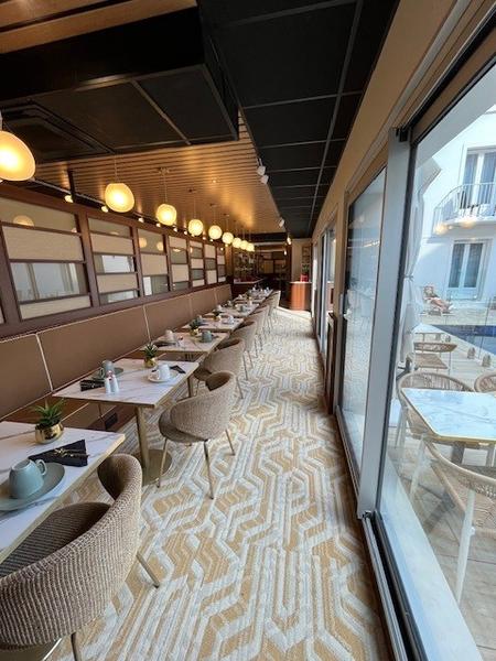 Une dizaine de tables et chaises avec banquettes dressées avec des tasses et couverts.