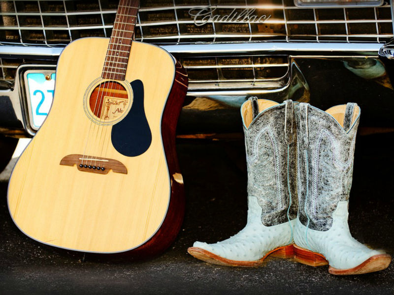 Une guitare avec des bottes de country posées devant une voiture