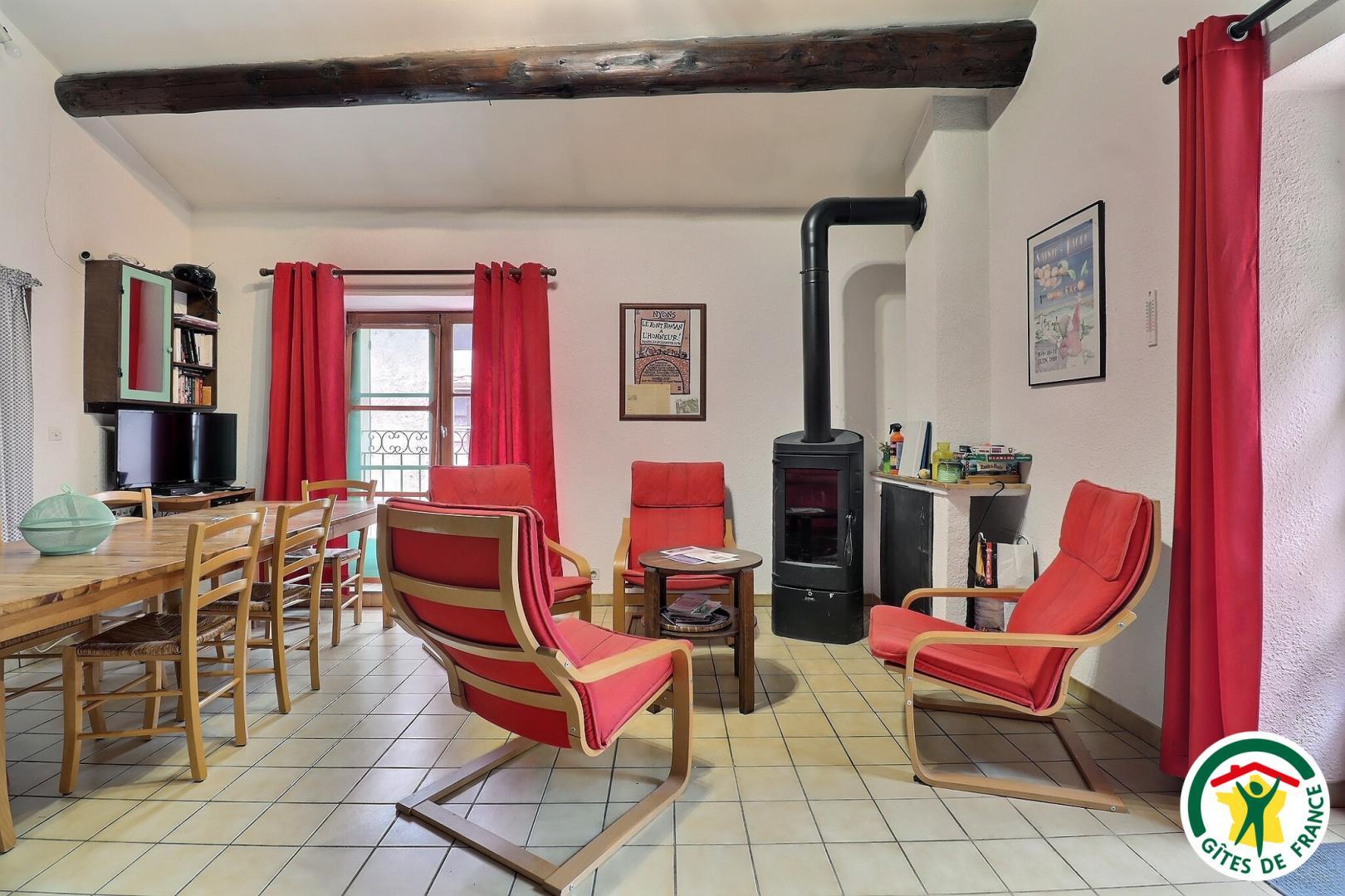 Pièce à vivre avec fauteuils, poêle à bois, espace repas et cuisine
