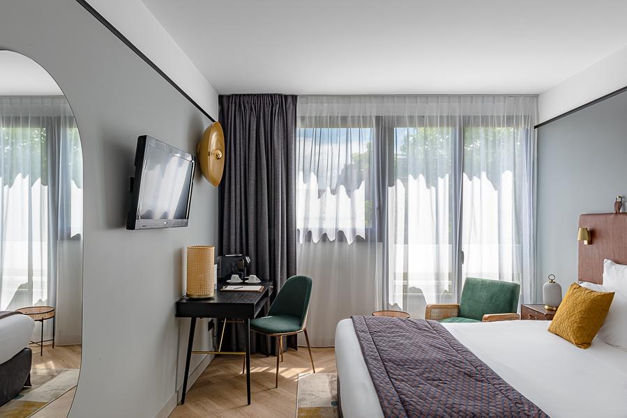 Une chambre grise avec un lit double, un bureau et une télévision.