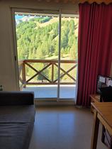 Séjour lumineux avec canapé, TV, ameublement bois, porte-fenêtre donnant sur un balcon avec vue sur les montagnes