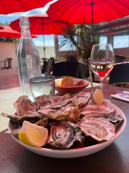 Une assiette d'huitres sous un parasol rouge, accompagné par une bouteille d'eau en verre et un verre de vin.