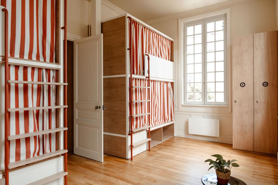 Un dortoir avec des lits superposés, fermés individuellement par des rideaux rayés rouge et blanc.