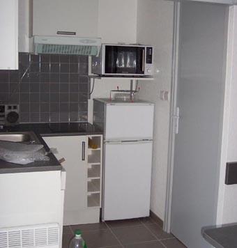 Cuisine avec frigo, plaques, hotte, rangement.