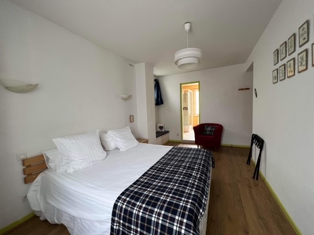 Chambre avec un lit double. Les murs sont blancs avec des cadres. A l'arrière plan, la porte de la salle de bain.