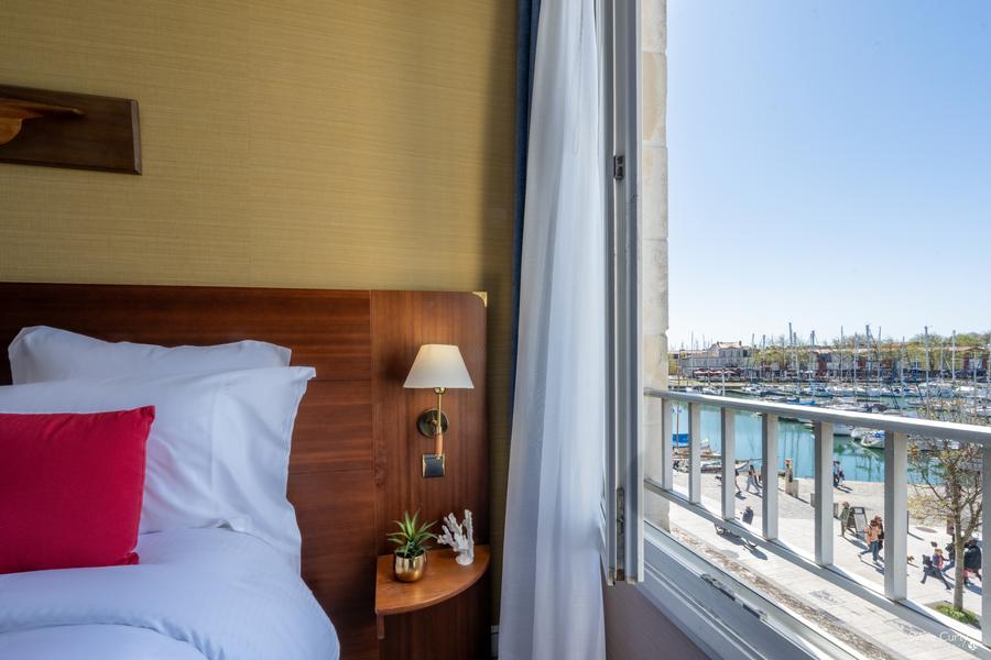 Zoom sur un bout de lit avec vue sur le vieux-port deuis la fenêtre ouverte.