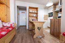 Séjour de studio avec canapé-lit, table à manger, coin cuisine, ameublement bois, porte vers les autres espaces