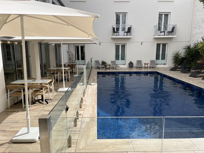 La piscine extérieure de léhôtel, avec des bains de soleils, et des tables et chaises sous des parasols.