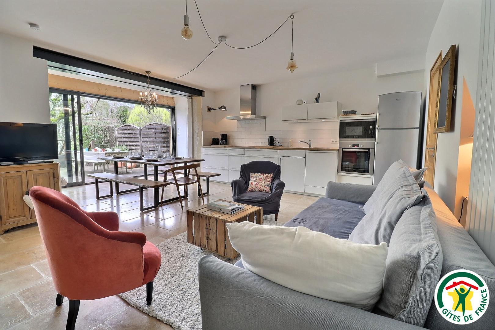 Pièce à vivre avec coin salon TV, poêle à bois, espace repas et cuisine équipée