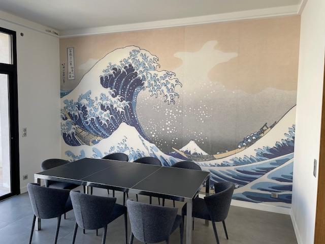 Table et chaise dans la salle à manger, au mur un papier peint de La Grande Vague de Kanagawa.