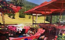 Terrasse extérieure du restaurant en été, tables et chaises en plastique, grands parasols, vue sur un champ et sur les montagnes