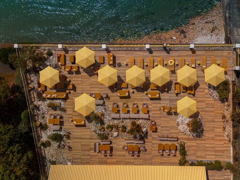 La terrasse en bord d'océan, avec des transats, parasols, tables, chaises, fauteuils, canapés, en vue aérienne.