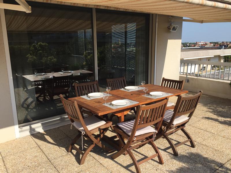 Table dressée pour 4 personnes sur le balcon, le store est déployé.